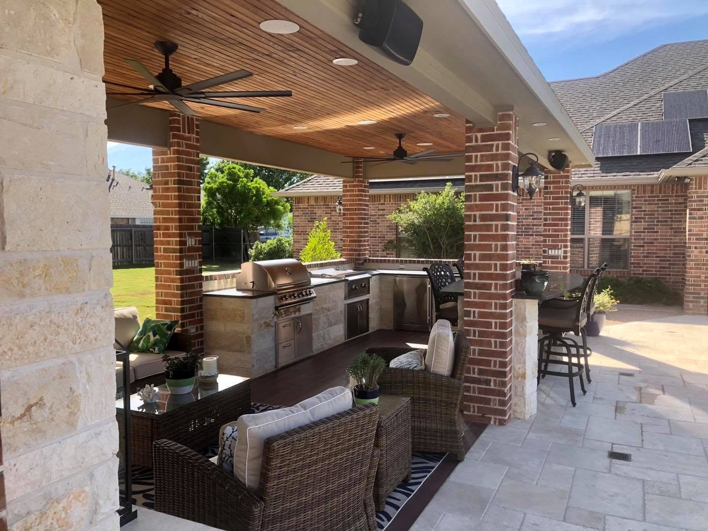 Covered outdoor living space with stone columns, wood ceiling, and outdoor kitchen built by WTX Landscape Design