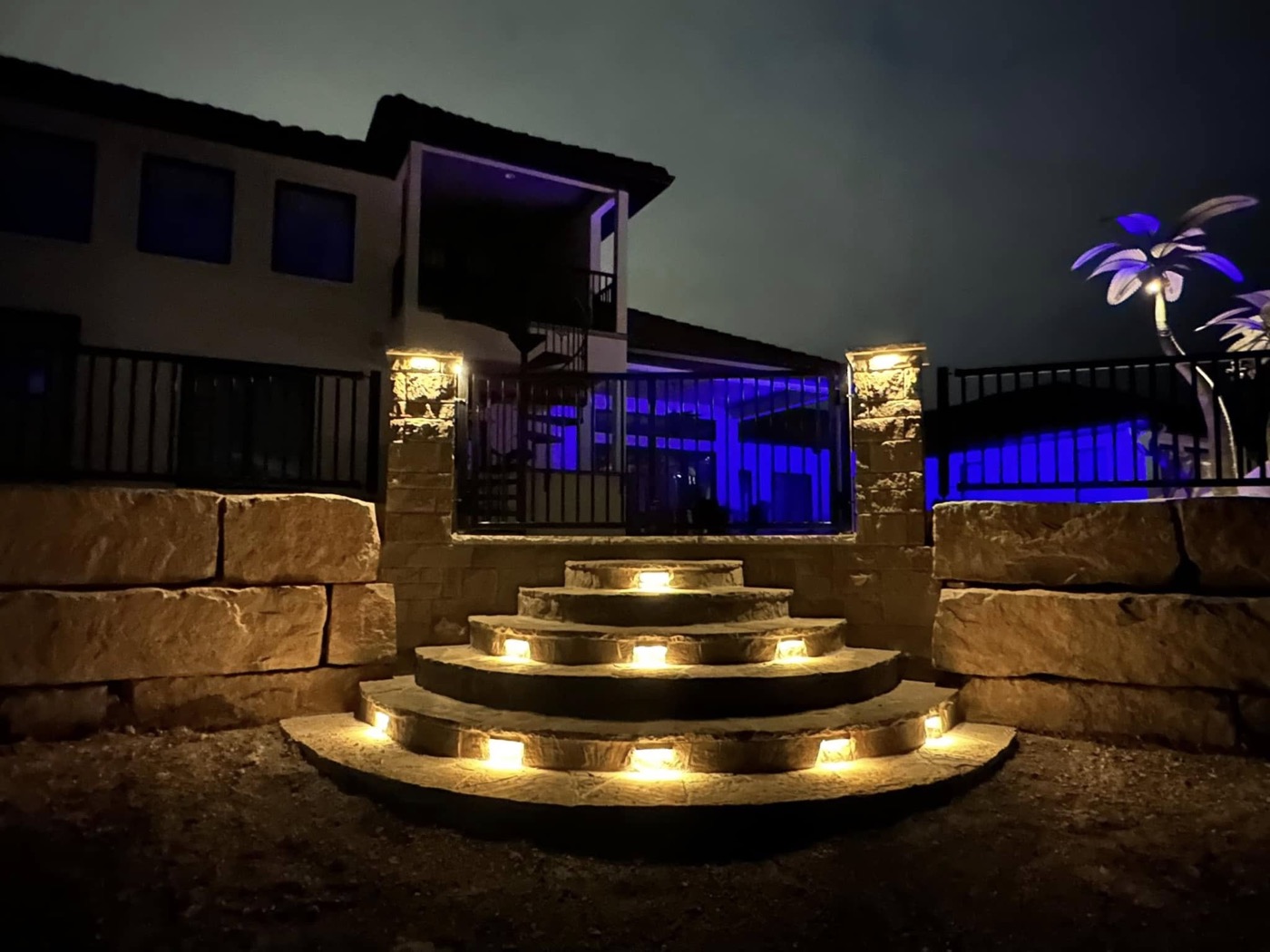 Curved stone steps glowing with built-in lighting at night, pool lit blue in the background