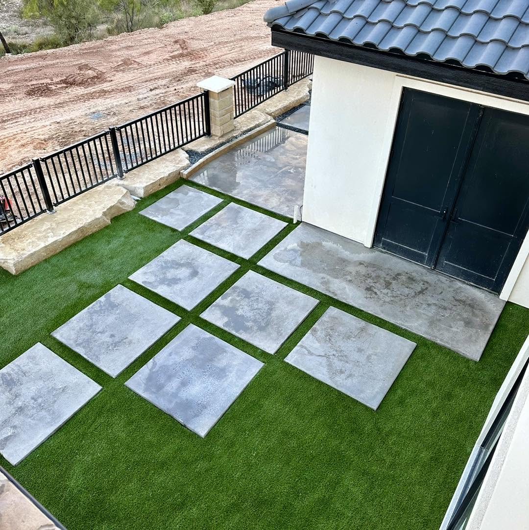 Large square concrete pavers set in bright synthetic turf beside a modern home