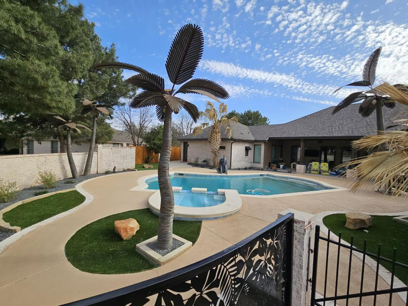 Backyard pool and raised spa with curved deck, turf islands, and sculpted metal palm trees