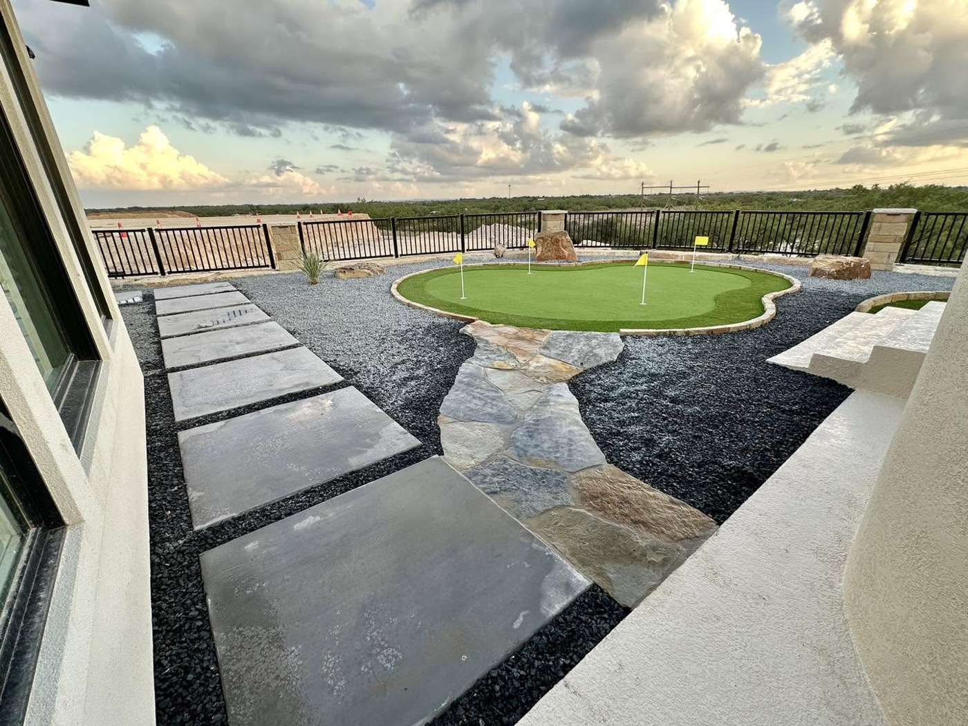 Backyard putting green ringed with gravel and a natural flagstone path, wide West Texas horizon behind