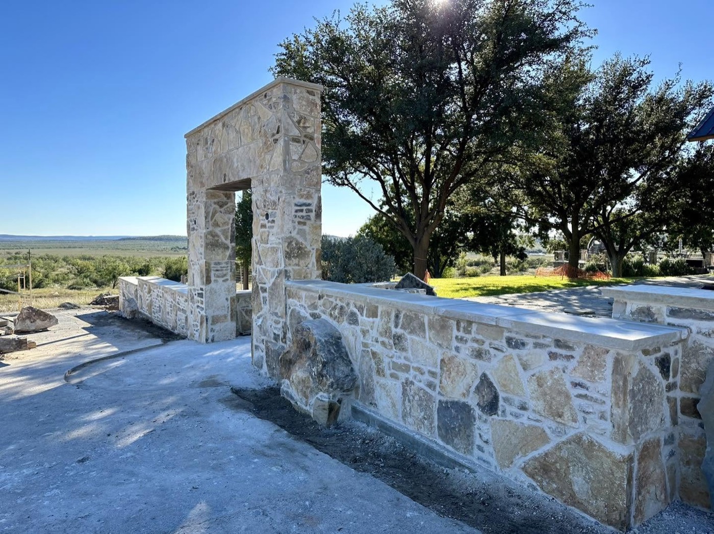 Limestone entry gateway and low perimeter wall with live oaks and open country beyond