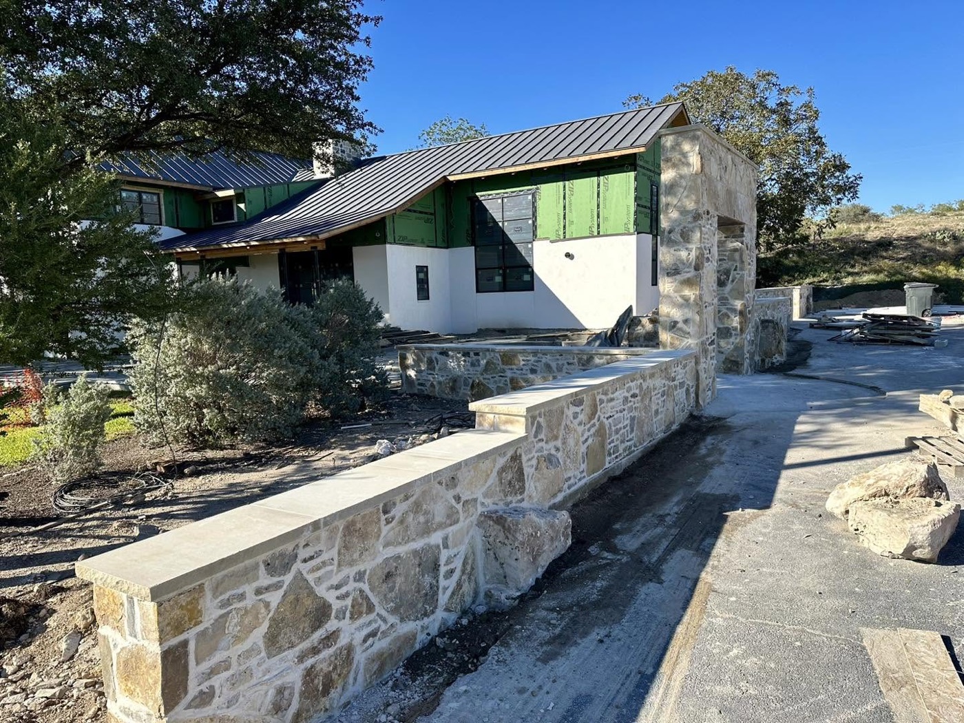Long limestone knee wall with cut-stone cap leading to the entry of a hill-country modern home